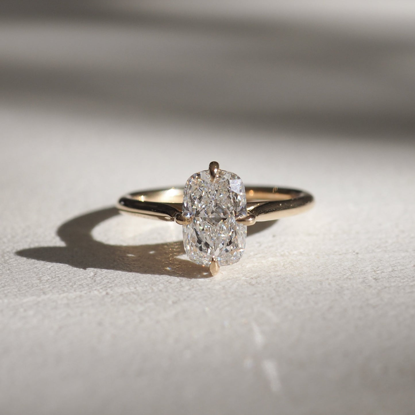 Oval diamond ring with a gold band, elegantly placed on a textured surface. The diamond catches light, highlighting luxury jewellery.