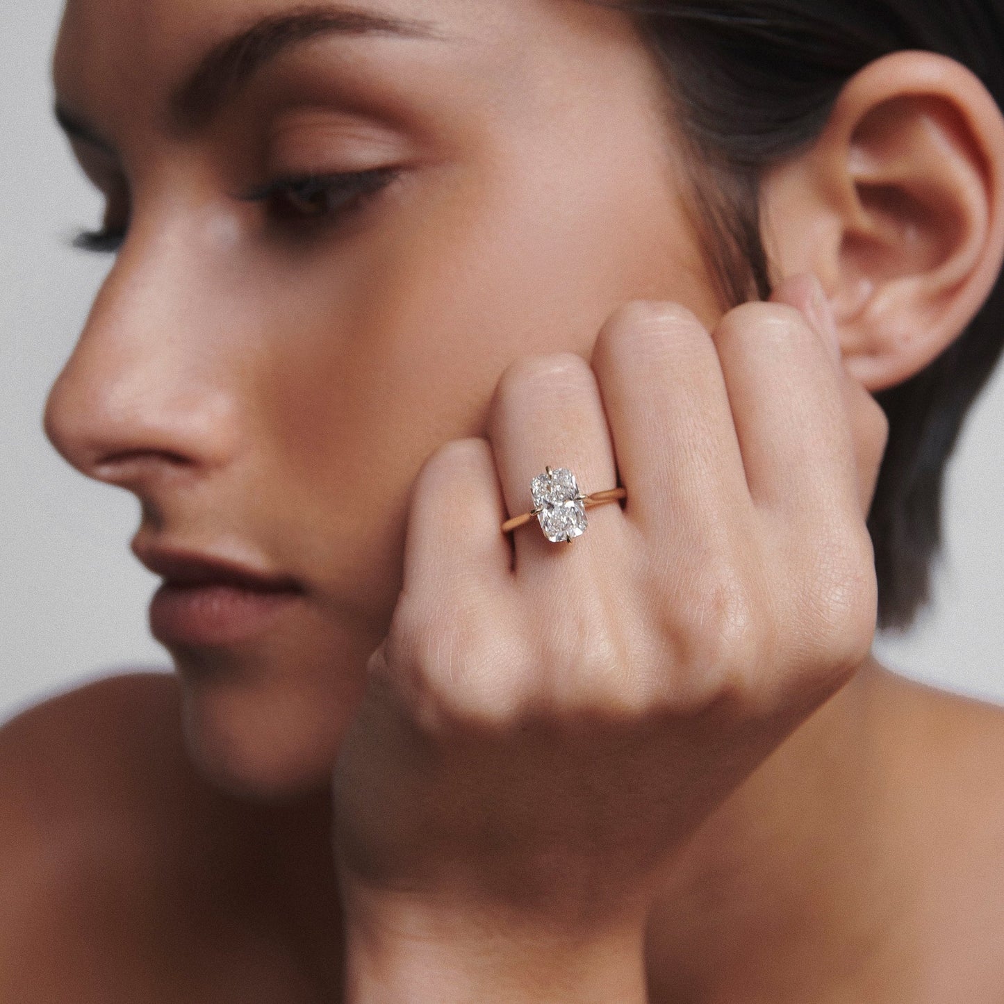 Woman showcasing an elegant, large oval diamond ring with a gold band, demonstrating luxury jewellery in a stylish setting.