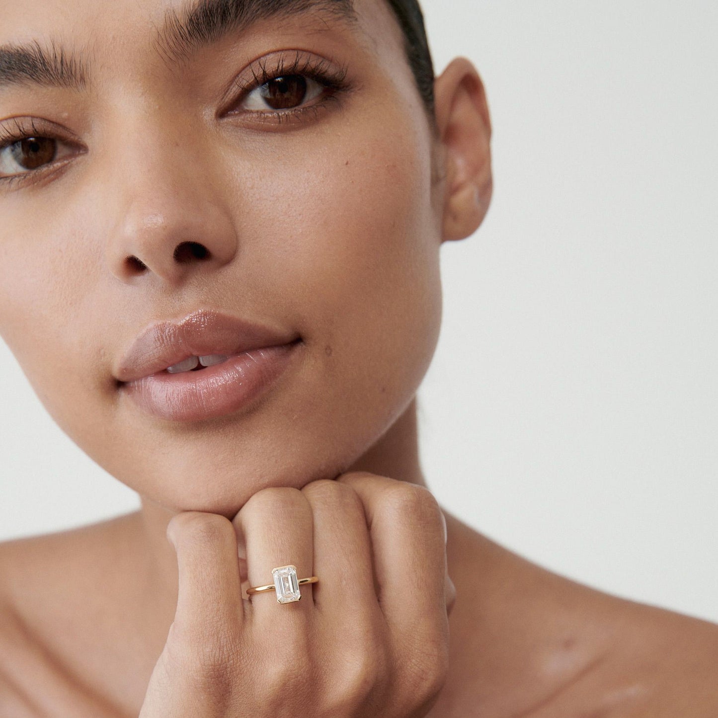 Woman showcasing an emerald-cut diamond ring on her finger. Close-up, minimalistic, luxury jewellery focus.