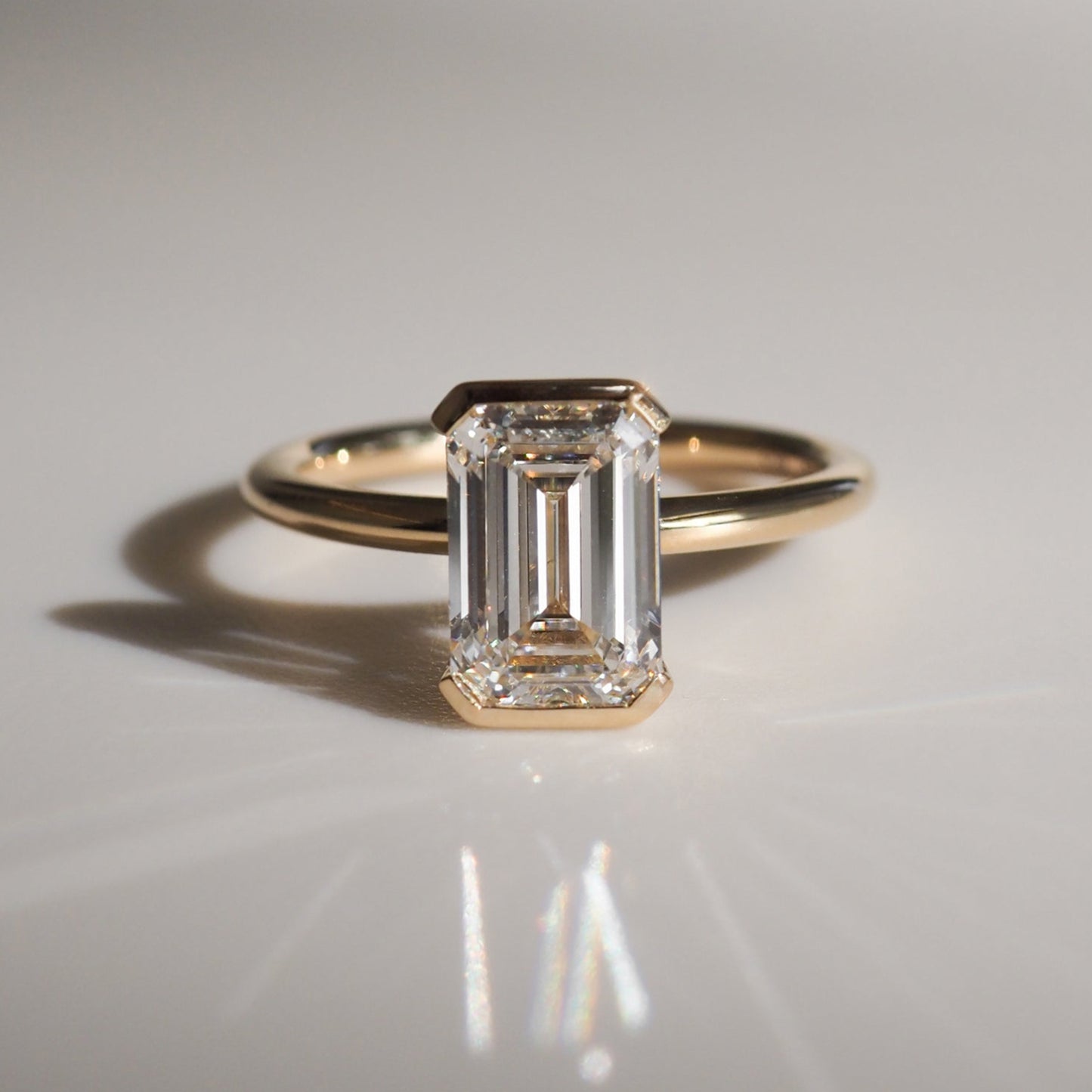 Emerald-cut diamond ring with a gold band, elegantly reflecting light on a smooth surface, highlighting luxury jewellery design.