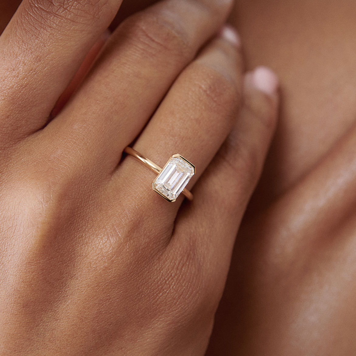 Elegant hand wearing a luxurious emerald-cut diamond ring on a slender gold band, highlighting high-end jewellery style.