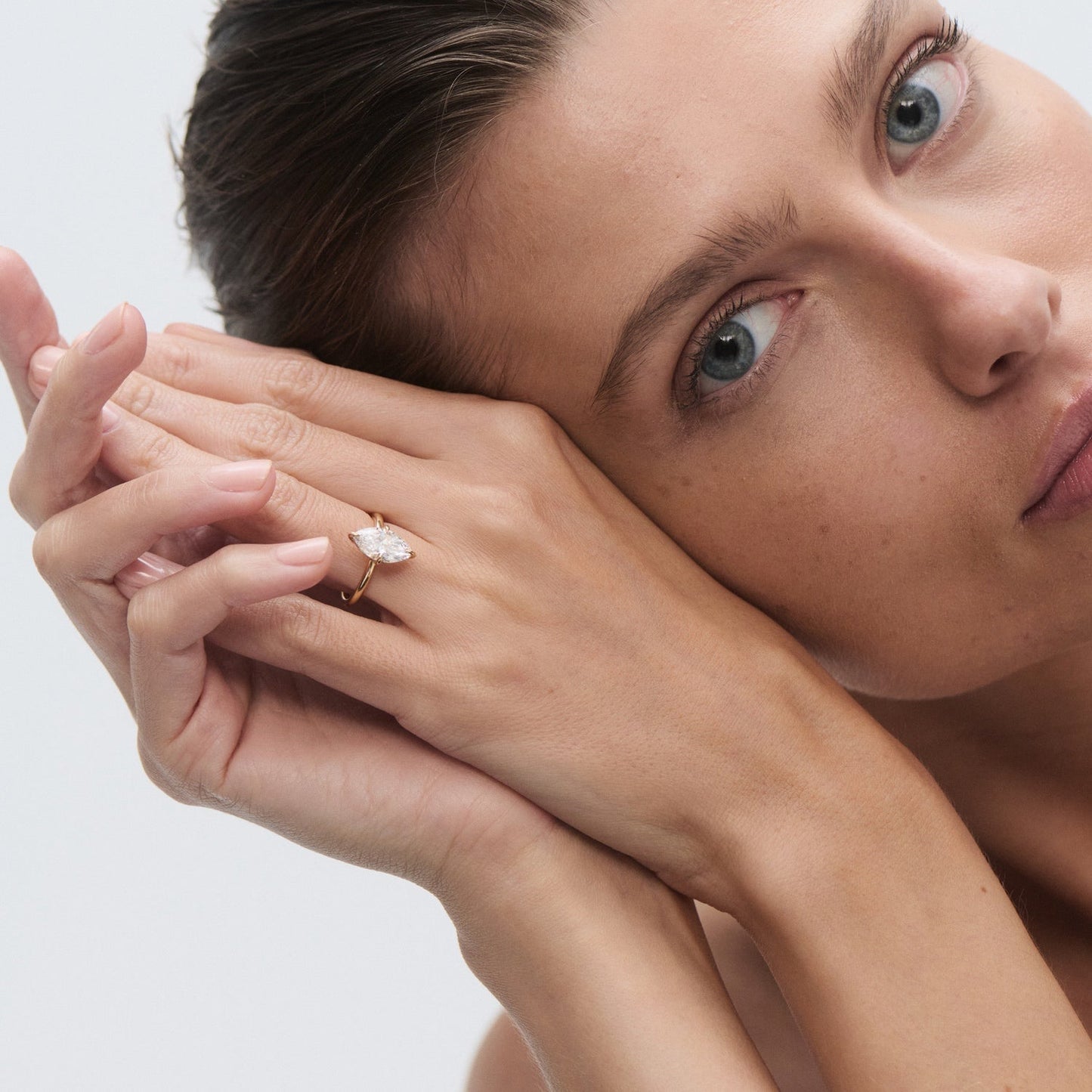 Woman showcasing a marquise-cut diamond ring on her finger, resting her face against her hands. Luxury jewellery, elegant style.