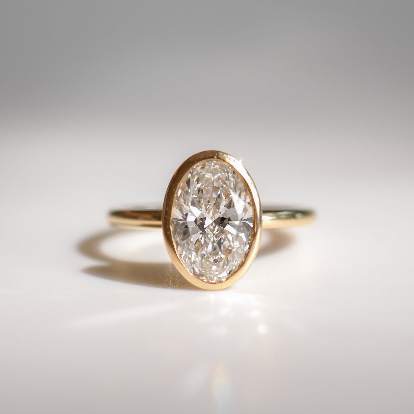 Gold ring featuring a prominent oval diamond, elegantly displayed on a reflective surface, evoking luxury and sophistication in fine jewellery.