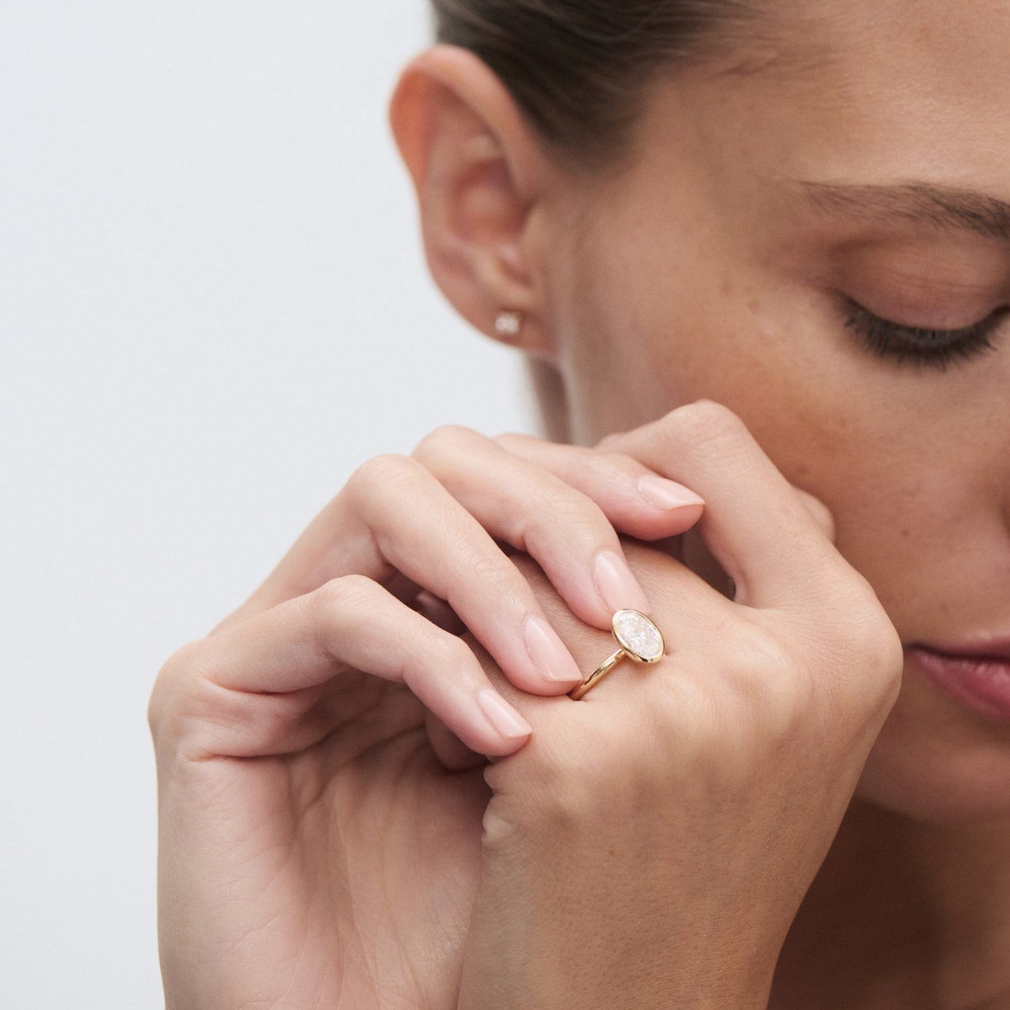 Woman admiring a gold ring featuring an oval gemstone, highlighting luxury jewellery. Minimalist design, subtle elegance, sophisticated style.