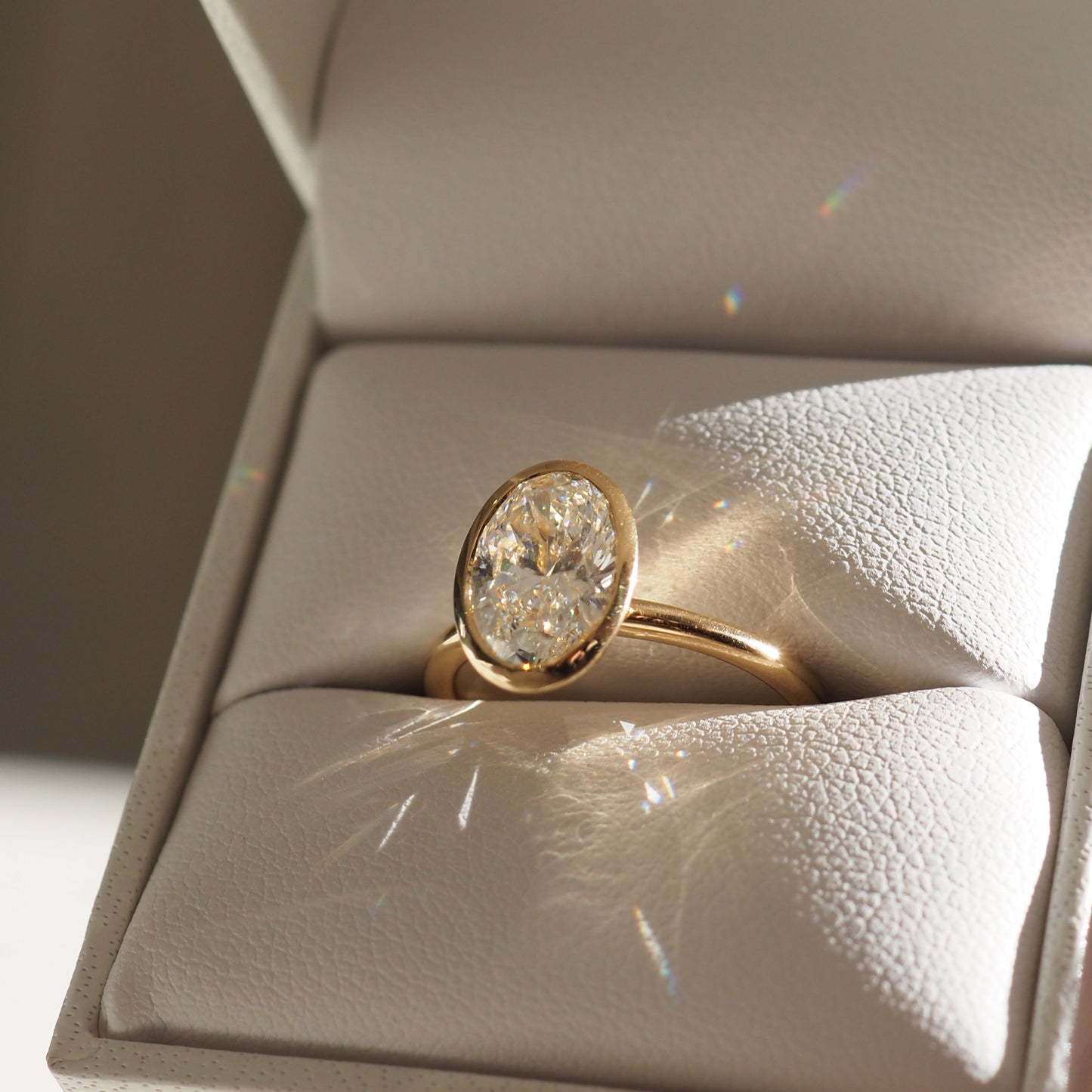 A gold band with an oval diamond ring displayed in an open white jewellery box, sparkling under soft light. Perfect for luxury engagements.