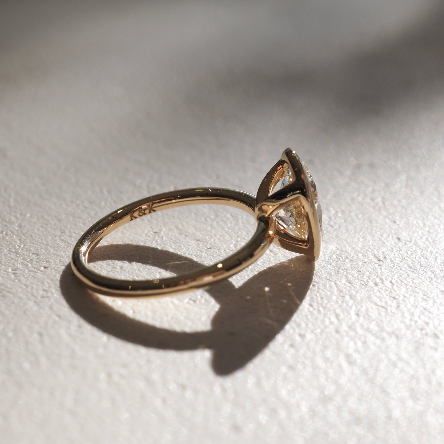 Gold engagement ring with a large central diamond, captured in soft light on a textured surface, casting a delicate shadow.