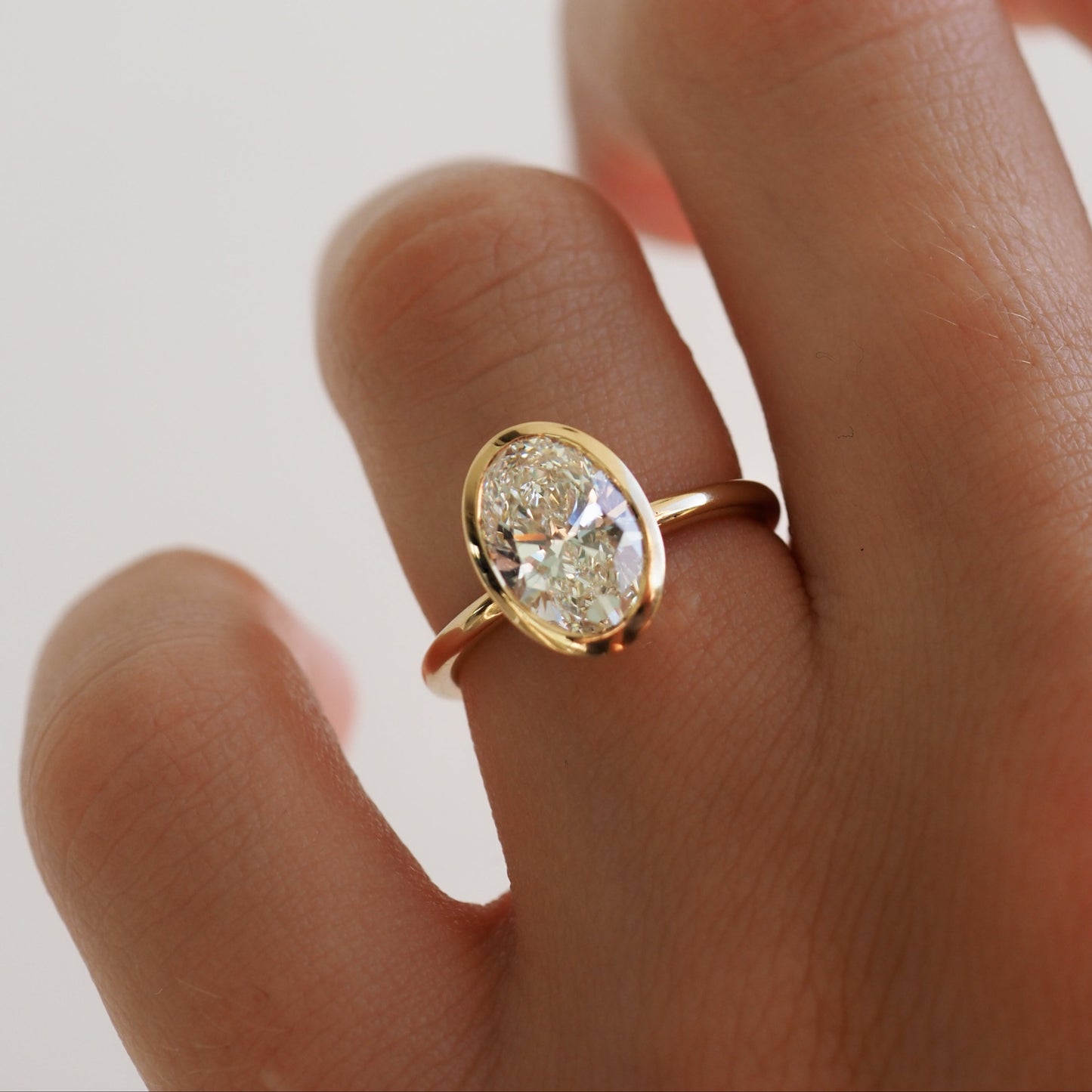 A hand wearing an elegant gold ring with a large oval diamond, showcasing luxury jewellery design against a soft, blurred background.