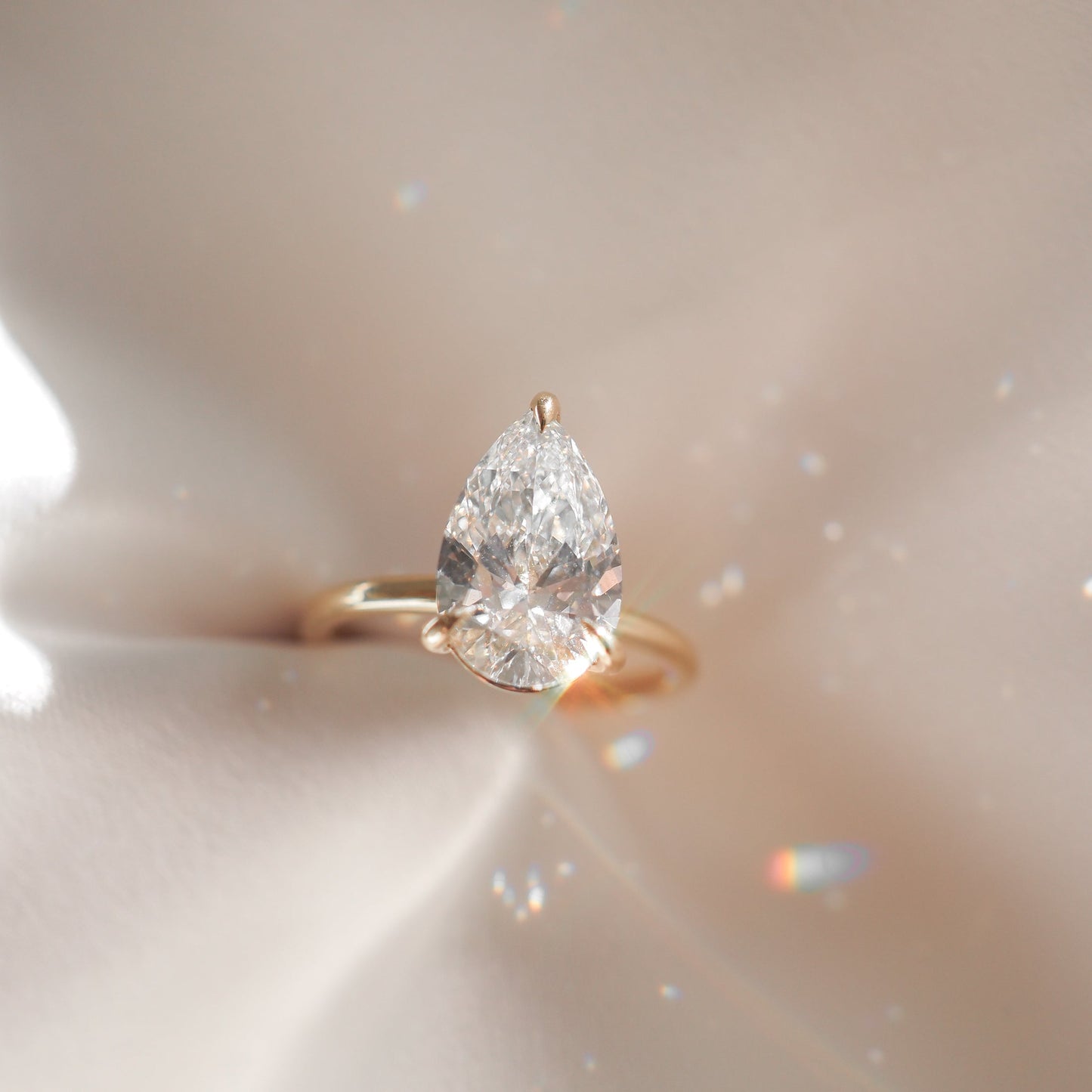 Pear-cut diamond ring with gold band on silky fabric, showcasing luxury jewellery sparkle and elegance.