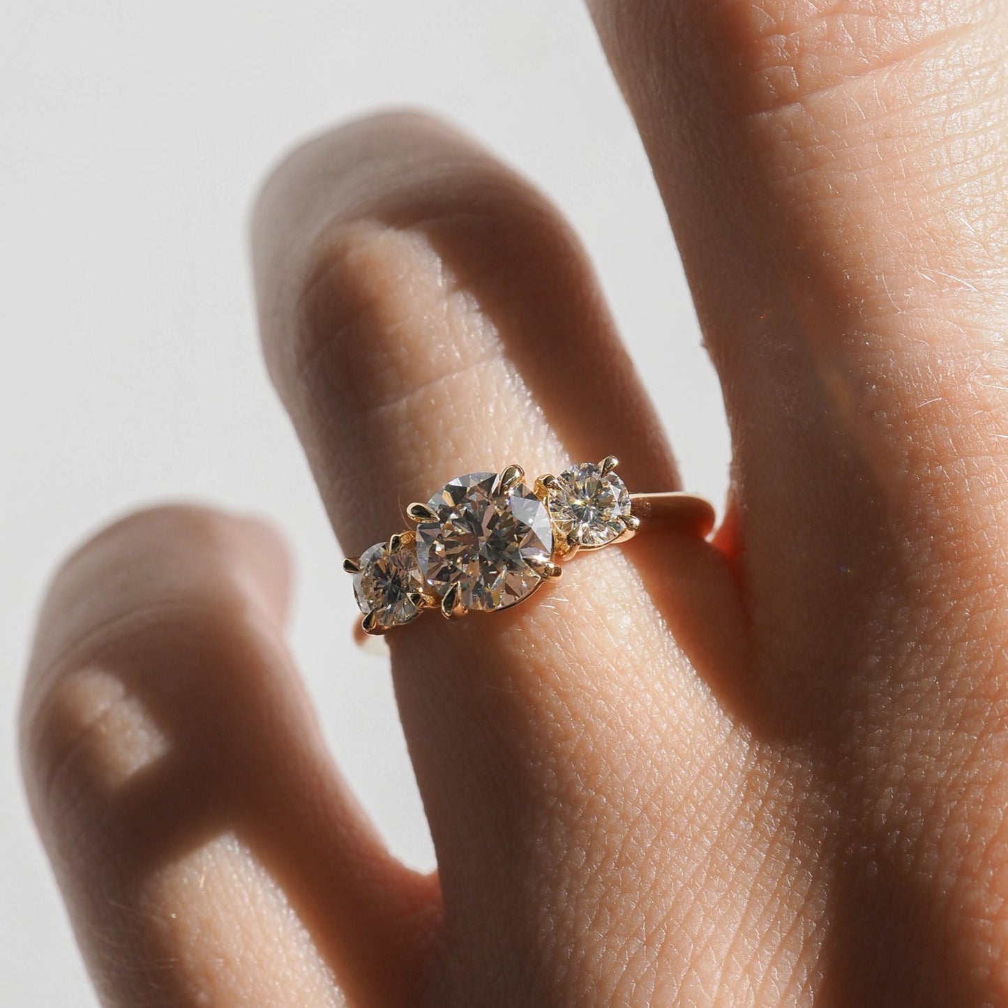 Hand with a three-stone diamond engagement ring; central round-cut diamond flanked by two smaller diamonds on a gold band.