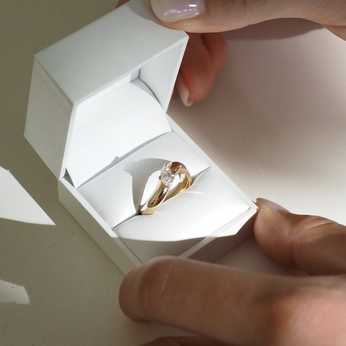 Hands holding a white box with a gold diamond engagement ring inside, highlighting luxury jewellery.