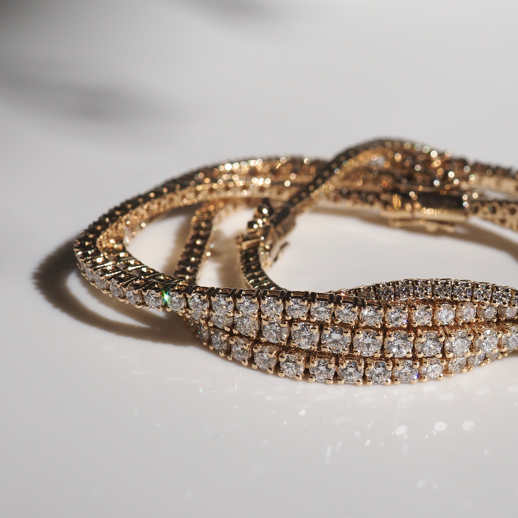 Elegant gold and diamond tennis bracelets on a white surface, glistening in natural light. Perfect for luxury jewellery enthusiasts.