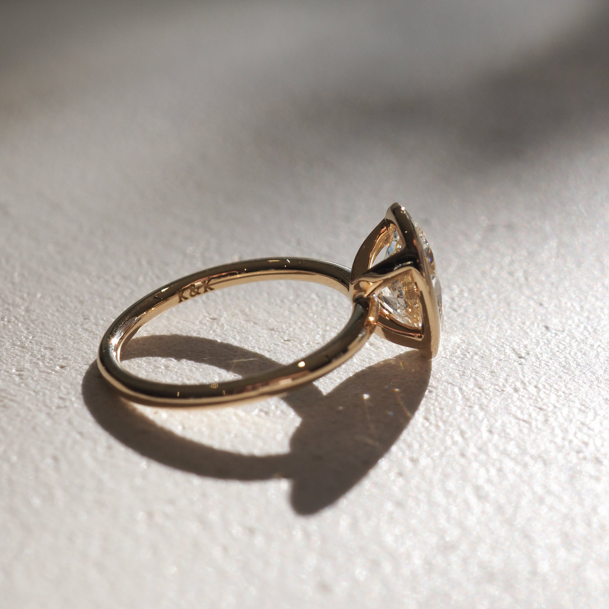 Gold engagement ring with a large central diamond, captured in soft light on a textured surface, casting a delicate shadow.