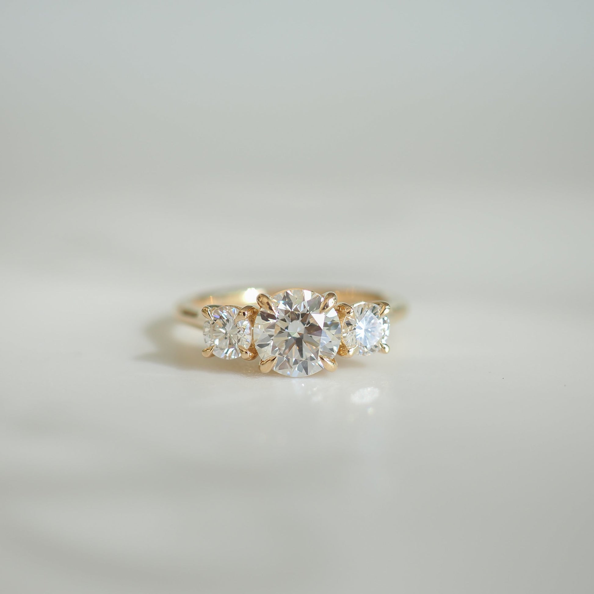 Elegant gold ring featuring four sparkling diamonds set in a symmetrical design against a soft, blurred background. Ideal for luxury jewellery lovers.